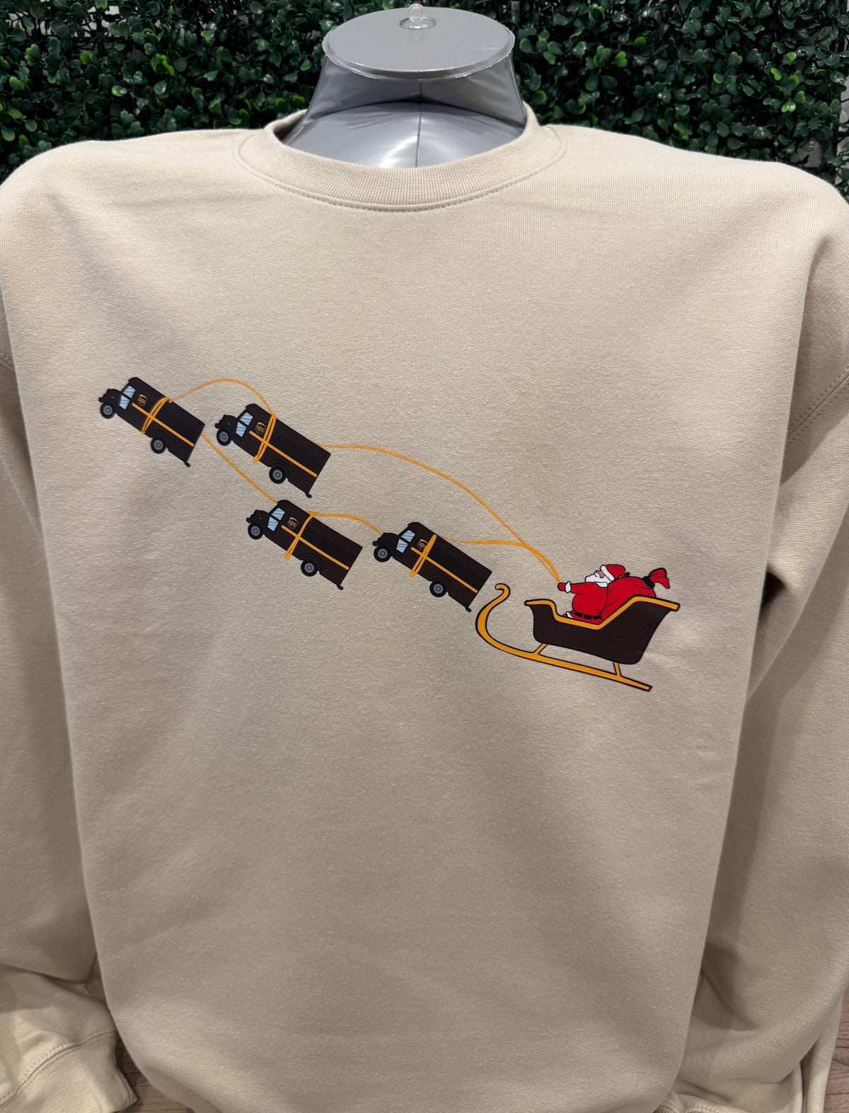 UPS Santa Peak Season beige crewneck sweater with graphic of Santa pulled by UPS trucks